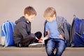 Primary education, school, friendship concept - two boys with backpacks sitting, talking and playing with spinner
