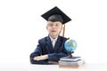 Primary school boy with large glasses and student hat sits at table, notebooks and glob . Quick learner. Isolated on white Royalty Free Stock Photo
