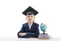 Primary school boy in school uniform with large glasses and student hat sits at table. Quick learner. Isolated on white background Royalty Free Stock Photo