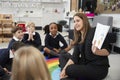 Primary school children sitting on the floor in the classroom with their teacher holding up a book to show them, selective focus Royalty Free Stock Photo