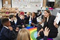 Primary school kids sitting on the floor in a classroom with their teacher, raising hands to answer a question, selective focus Royalty Free Stock Photo