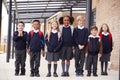 Primary school kids standing in a row on a walkway outside their school, smiling to camera, low angle