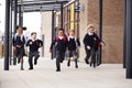 Primary school kids, wearing school uniforms and backpacks, running on a walkway outside their school building, front view