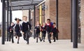 Primary school kids, wearing school uniforms and backpacks, running on a walkway outside their school building, front view