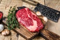 Prime rib eye raw beef meat steak on a butcher wooden cutting board with cleaver. wooden background. Top view