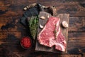 Prime T-bone beef meat steak, raw porterhouse steak on butcher board with herbs. Wooden background. Top view Royalty Free Stock Photo