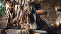 Primeval Caveman Wearing Animal Skin Trying to make a Fire with Bow Drill Method. Neanderthal Kind Royalty Free Stock Photo