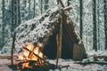 Primitive survival shelter in winter forest with Christmas garland near campfire