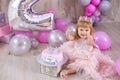 Princess baby girl celebrating life event wearing golden crown and pink airy dress. Cute girl posing in pastel colors studio shoot