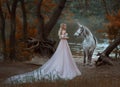 The princess met a unicorn in the forest. The blonde girl with a gentle make-up, is dressed in a long vintage dress with Royalty Free Stock Photo