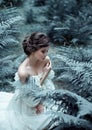 The princess sits on the ground in the forest, among the fern and moss. An unusual face. On the lady is a white vintage