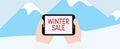 Winter sale banner. Hands holding tablet with WINTER SALE text on Blue mountains with snow background