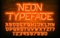 Neon alphabet typeface. Futuristic orange neon letters and numbers. Brick wall background.