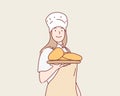 Female baker holding a table with several breads smiling a lot