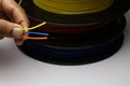 Printer Filaments spool laid horizontally with three different color filament held in hand. Material produced from poly-lactic