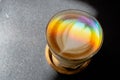 A prism dispersing sunlight splitting into a spectrum on coffee cup with heart shape latte art foam on black table.