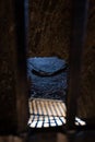 A prison cell with a hammock and sun rays penetrating through the locked bars