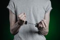 Prison and convicted topic: man with handcuffs on his hands in a gray T-shirt and blue jeans on a dark green background in the stu Royalty Free Stock Photo