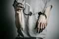 Prison and convicted topic: man with handcuffs on his hands in a gray T-shirt on a gray background in the studio, put handcuffs on