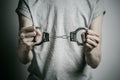 Prison and convicted topic: man with handcuffs on his hands in a gray T-shirt on a gray background in the studio, put handcuffs on