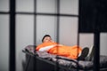 A prisoner in an asian high-security prison lies on a bunk in a red prisoner`s uniform in a solitary cell.