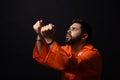 Prisoner in jumpsuit with handcuffs praying on black background