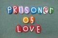 Prisoner of Love, creative slogan composed with multi colored stone letters over green sand