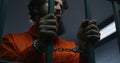 Prisoner in orange uniform and handcuffs holds metal bars