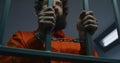 Prisoner in orange uniform and handcuffs holds metal bars