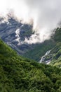 Pristine stream winds its way between majestic green mountains hidden in clouds. Norway