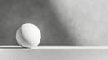 Minimalist still life featuring a white sphere balancing on the edge of a white table against a gray background, evoking Royalty Free Stock Photo