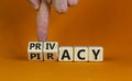 Privacy vs piracy symbol. Businessman hand turns cubes and changes the word `piracy` to `privacy`. Beautiful orange background