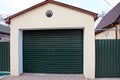 Garage with closed green gates and part of the fence in the street near the road