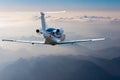 Private jet, passenger wide-body plane or aircraft is flying in the blue sky over the the clouds and mountains. Summer Royalty Free Stock Photo