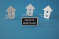 Private mortgage symbol. Wooden houses sits next to a wooden black board with the word Private mortgage. Beautiful blue background