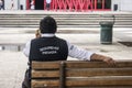 A private security guard sitted in a bench in a park talking in the phone.