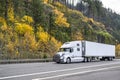 Pro industrial big rig white semi truck with grille guard transporting cargo in refrigerated semi trailer driving on the autumn Royalty Free Stock Photo