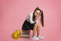 Problems in school education. Sad little schoolgirl in glasses with backpack sits on pile of books