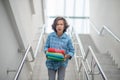 Upset schoolboy walking downstairs, carrying pile of books