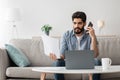 Problems at work. Arab man discussing documents, holding paper and talking on cellphone, working remotely at home Royalty Free Stock Photo