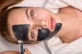 Procedure for applying black mask on face of beautiful woman, top view. Spa treatments Royalty Free Stock Photo