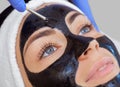 The procedure for applying a black mask to the face of a beautiful woman.