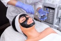 The procedure for applying a black mask to the face of a beautiful woman. Royalty Free Stock Photo