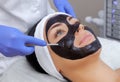 The procedure for applying a black mask to the face of a beautiful woman. Royalty Free Stock Photo