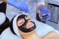 The procedure for applying a black mask to the face of a beautiful woman. Royalty Free Stock Photo