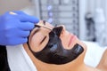 The procedure for applying a black mask to the face of a beautiful woman. Royalty Free Stock Photo