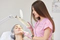 Procedure of facial skin examination at cosmetology clinic. Portrait of young woman with closed eyes, specialist in medical gloves