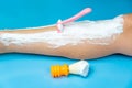 The procedure for hair removal of the legs with a pink disposable razor on a blue background, next to it is an orange shaving