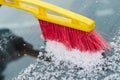 The process of cleaning the windshield of the car from the snow with a red and yellow brush