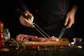 The process of cooking beef steak on the kitchen table for barbecue with aromatic spices. Fork and knife in the hands of a cook Royalty Free Stock Photo